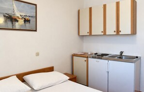 Une petite pièce comprenant un lit, un coin cuisine et un tableau accroché au mur.