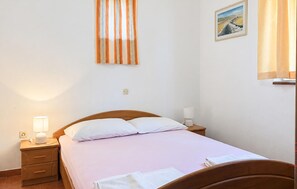 Ein Einzelbett mit Holz-Kopfstück, ein Nachttisch mit Lampe, ein Wandbild und ein Fenster mit Vorhängen.