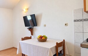Ein Essbereich mit einem Tisch, gedeckt für zwei Personen, einem an der Wand befestigten Fernseher und einer Obstschale auf dem Tisch.