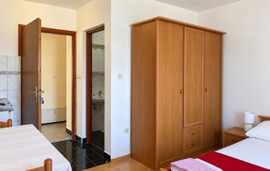 Ein Schlafzimmer mit einem Bett, einem Nachttisch, einem Holzschrank und einem durchgegangenen Türrahmen einsehbaren Badezimmer.