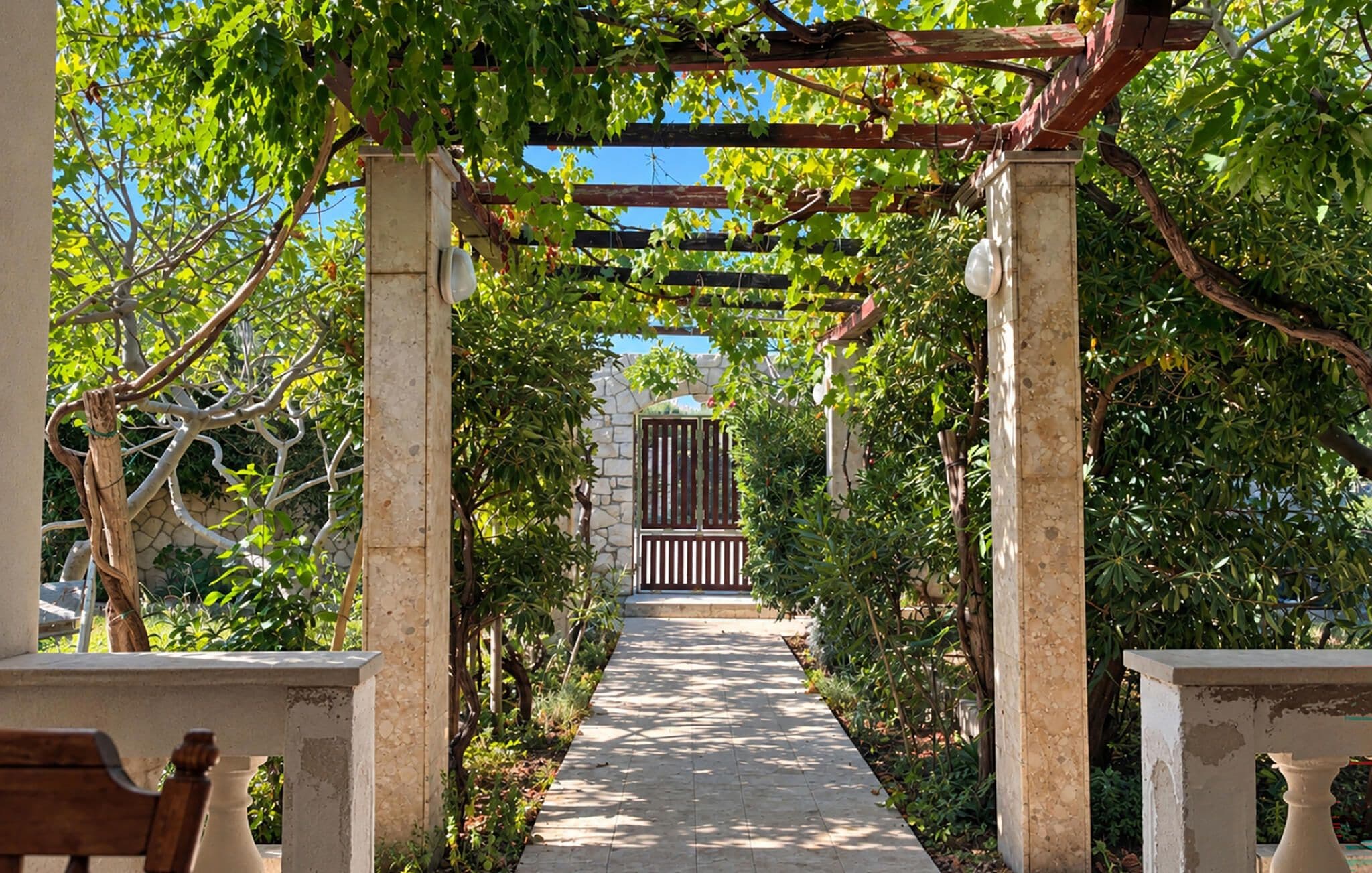 A pathway leading to a gated entrance, flanked by stone pillars and greenery.