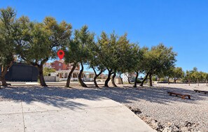 A paved walkway with trees and benches, a building with balconies, and a clear blue sky. - Nice apartment in Razanac with WiFi (Razanac)
