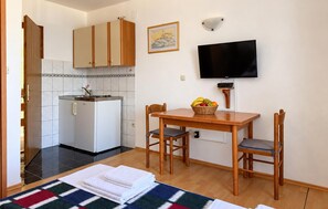 Una cuina compacta amb un frigorífic, un rentapeus i un microones. Hi ha una zona de menjador amb una taula i caires, i una televisió penjada a la paret.