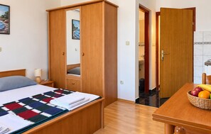 Ein Hotelzimmer mit einem Bett, einem Kleiderschrank, einem Spiegel, einem Nachttisch mit Lampe und einer Obstschale auf einem Holztisch.