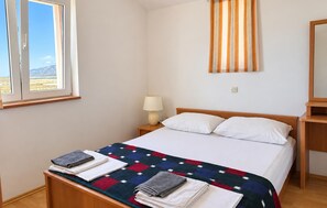 A hotel room with a bed, a nightstand, a lamp, a window with a view of mountains, and a striped curtain. - 1 bedroom lovely apartment in Razanac (Razanac)