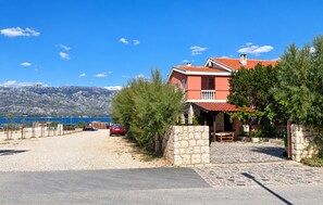 A coastal property with a stone wall, a red car parked in front, and a view of the sea and mountains in the background. - 1 bedroom lovely apartment in Razanac (Razanac)