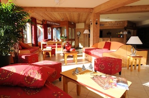 A cozy room with wooden walls, a sofa, a table with a map, and a clock on the wall. - Au pied des pistes | Piscine intérieure chauffée (Aussois)