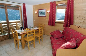 Ein gemütliches Zimmer mit einem Holztisch, Stühlen, einer Couch und einem Fenster mit Blick auf die Berge.