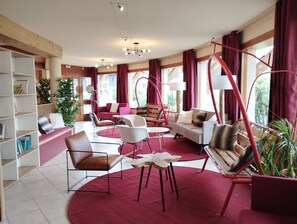 A modern living room with a red carpet, multiple seating options, and large windows. - Au pied des pistes | Piscine chauffée | Balcon (Aussois)