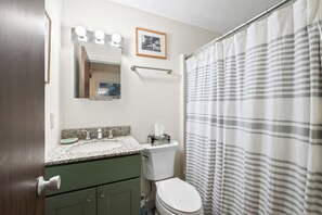 Ein Badezimmer mit Waschbecken, Spiegel, Toilette und Duschvorhang.