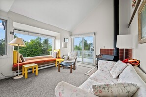 Ein Wohnzimmer mit einer Couch, einem Sessel und einem kleinen Tisch. Ein Fenster bietet Blick auf Grünflächen.