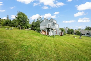 A two-story house with a balcony, surrounded by a grassy field and trees. - White Birch 60 | Ski in/Ski out! (Sandy River Plantation)