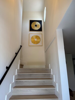A staircase with wooden steps and white walls, leading to a landing with two framed golden circular designs. - Spacious House W/Deck - Near FLL Airport, Beach, Dania Pointe & Hard Rock (Dania Beach)