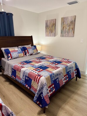 A bed with a quilt, a bedside lamp, and two wall art pieces. - Spacious House W/Deck - Near FLL Airport, Beach, Dania Pointe & Hard Rock (Dania Beach)