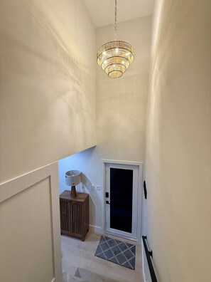 A narrow hallway with a chandelier, a door, and a small wooden cabinet. - Spacious House W/Deck - Near FLL Airport, Beach, Dania Pointe & Hard Rock (Dania Beach)
