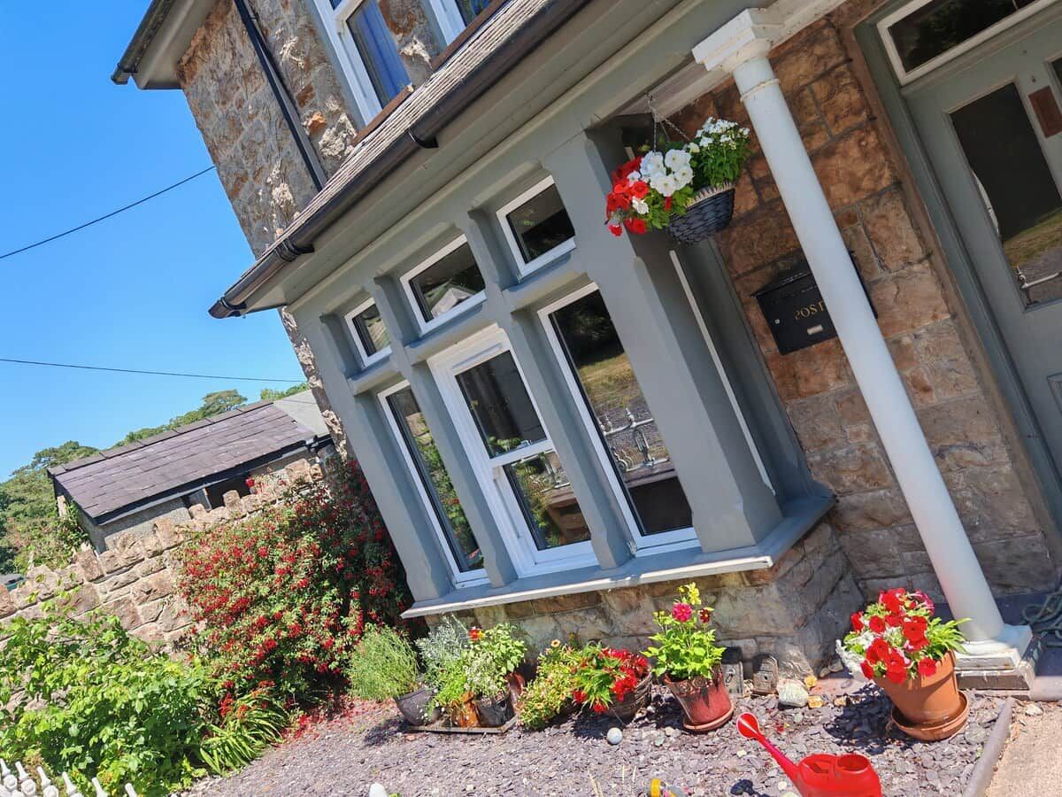 A stone building with multiple windows and a porch area with potted plants.