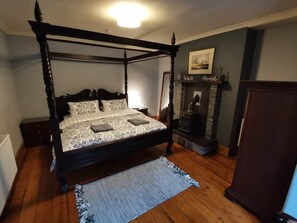 A four-poster bed with a patterned bedspread, a fireplace, and a wooden floor.