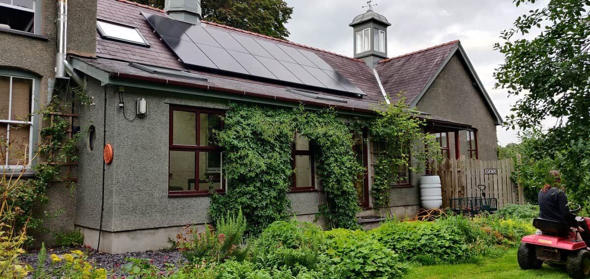 Una casa con techo de paneles solares, un jardín y una persona cortando el césped.