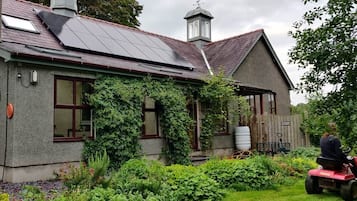 Una casa con techo de paneles solares, un jardín y una persona cortando el césped.