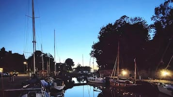 Un puerto deportivo con barcos amarrados, agua tranquila y árboles al fondo.