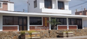 A building with a sign that reads 'RACS Hospedaje' and a stone wall with planters. - R. A. C. S. (Paracas-Paracas,)