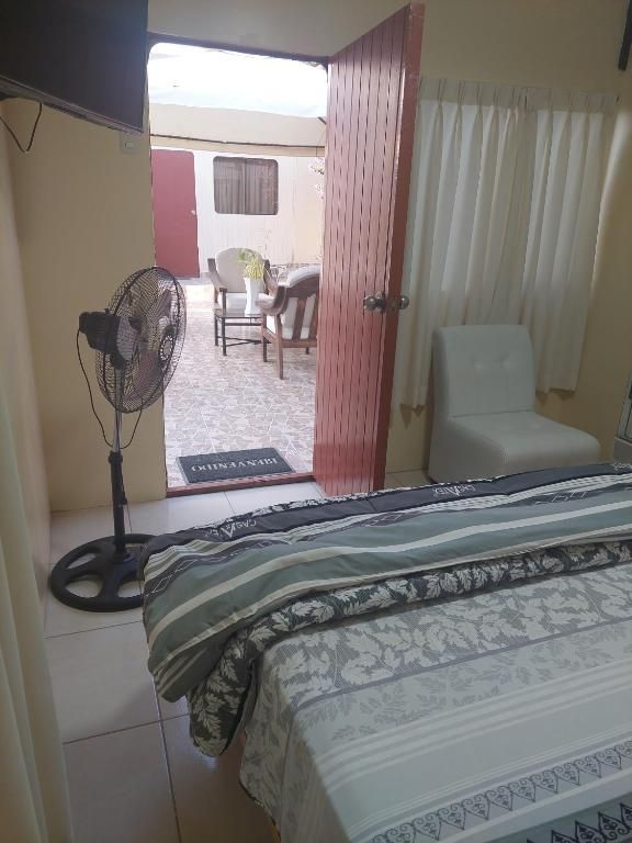 A bedroom with a bed, a fan, a chair, and a view of an outdoor area.
