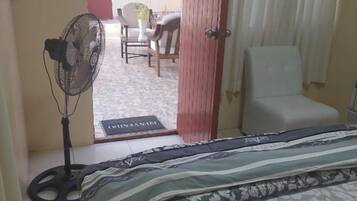 A bedroom with a bed, a fan, a chair, and a view of an outdoor area.