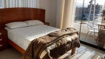A hotel room with a bed, a window with curtains, and a view of the city.
