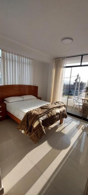 A hotel room with a bed, a window with curtains, and a view of the city. - R. A. C. S. (Paracas-Paracas,)