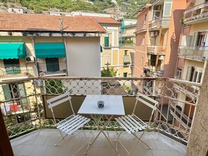 Een balkon met een tafel en stoelen, met uitzicht op een woongebied met terracottadaken en balkons.
