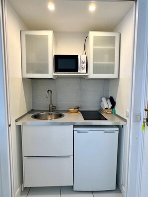 Een kleine keuken met een magnetron, spoelbak en bergkasten.