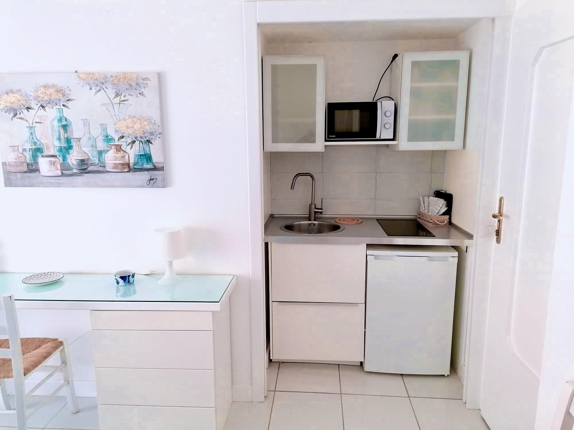 Une cuisine compacte équipée d’un four à micro-ondes, d’un évier et d’un petit réfrigérateur. On y trouve une table à manger avec des chaises et un tableau accroché au mur.