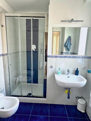 Een badkamer met een glazen douchecabine, een witte wastafel en een toilet met douchefunctie.