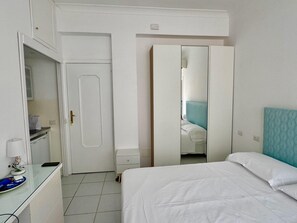 Et hotelværelse med seng, sengebord, spejl, garderobeskab og et lille skrivebord med lampe.