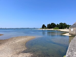 Klarer Blick auf einen Fluss mit Booten, einen Sandstrand und ein Steinhaus.