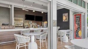 A modern bar area with white wicker chairs, a bar counter with various bottles, and a chalkboard menu. - Spacious 3BR Poolside Villa at Marriott's Crystal Shores (Marco Island)