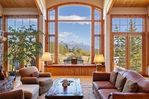 Ein gemütliches Wohnzimmer mit großem Fenster und Blick auf die Berge, Holzmöbel und einem Kamin.