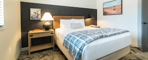 Ett hotellrum med en säng, sängbord, en lampa, en tavla på väggen och en dörr.