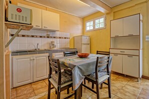 Eine kompakte Küche mit weißen Schränken, einer Kaffeemaschine, einem Kühlschrank und einem Esstisch mit Stühlen.