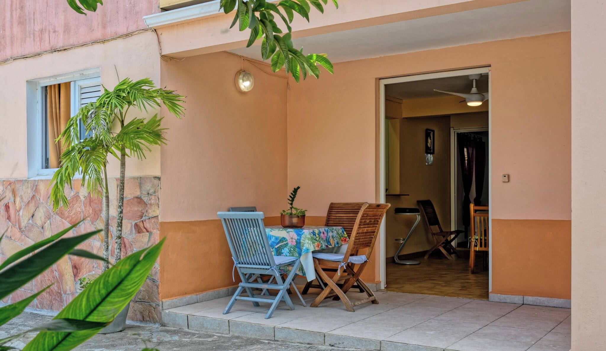 An outdoor seating area with a table and chairs, a potted plant, and a door leading to an interior space.