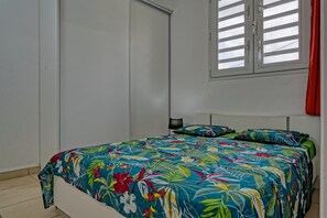 A bedroom with a bed, a window with blinds, a nightstand, and a lamp. - Colombe vanille - Terrasse - Wifi (Rivière-Salée)