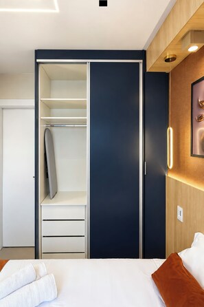 A modern bedroom with a built-in wardrobe, a bed with white linens, and a wooden accent wall. - Stay Home Itaim - Piscina - Academia (São Paulo)