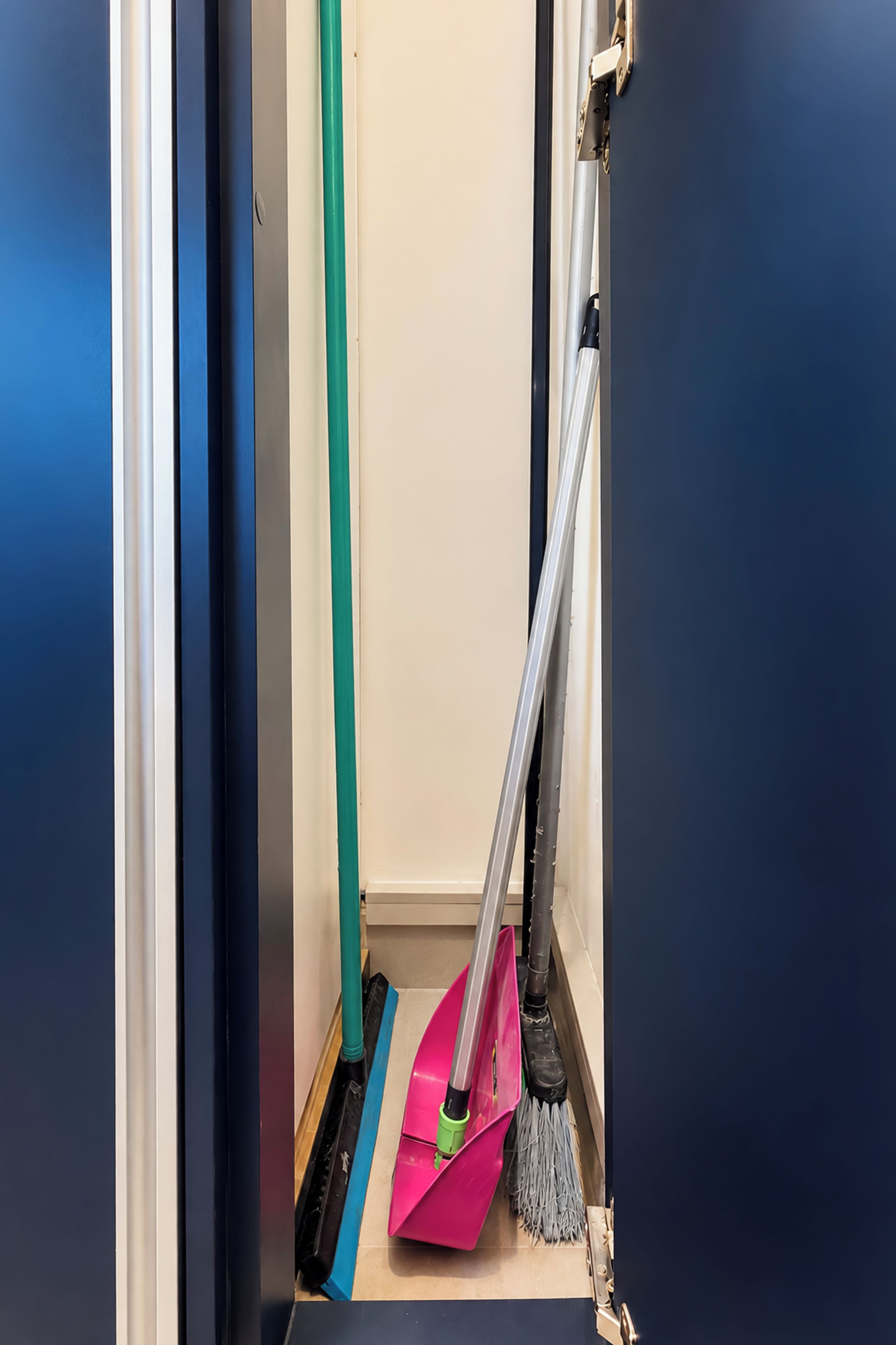 En hall med en kvast och en sopskyffel lutade mot väggen, en dörrkarm och en blå golvmatta.
