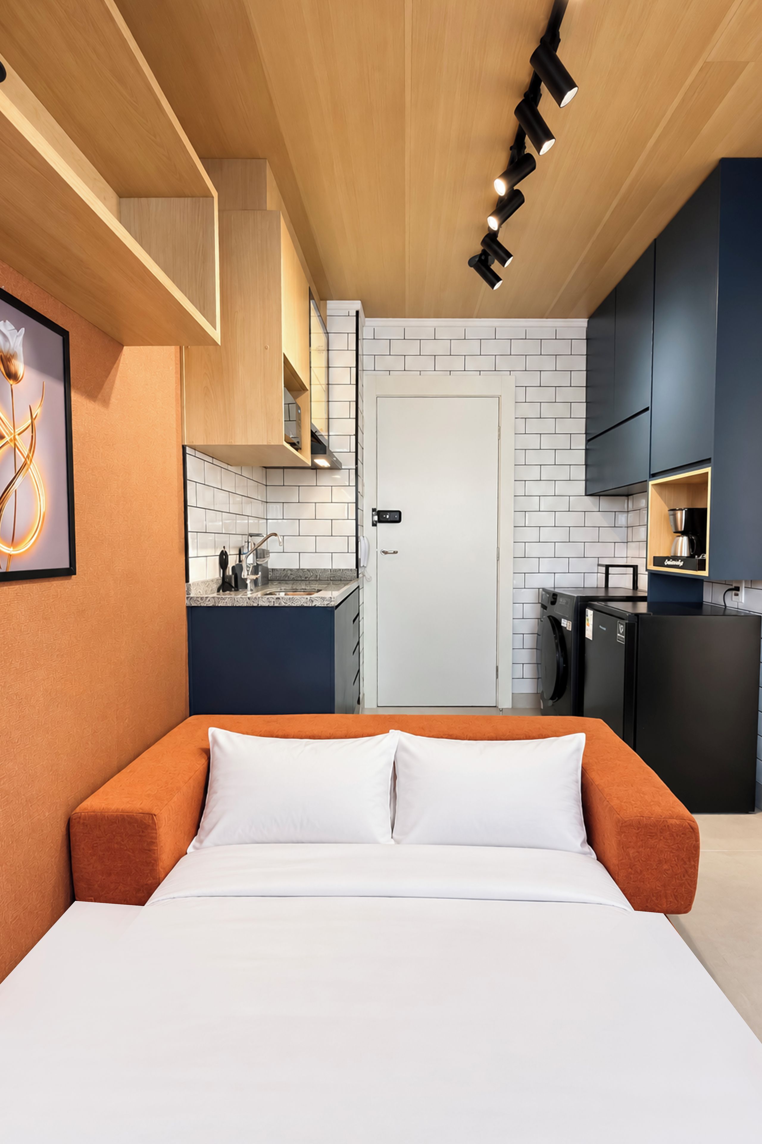 Quarto compacto com cama, cozinha compacta e pequena área de refeições.