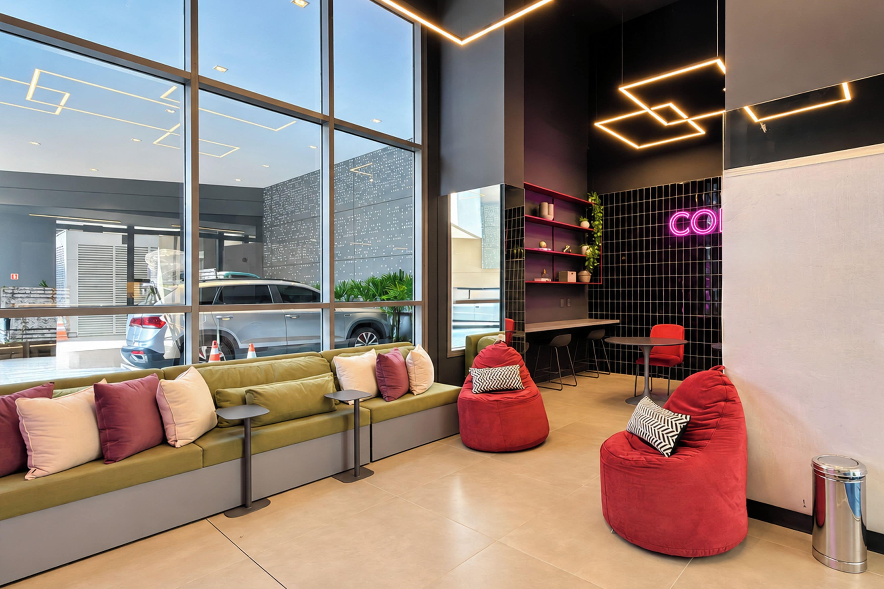 Um interior moderno com um sofá verde, poltronas de espuma vermelhas e um letreiro de neon.