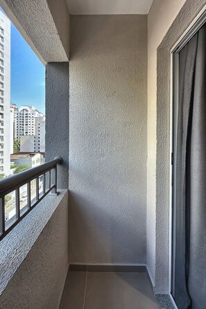 A balcony with a textured wall, a metal railing, and a view of buildings. - Stay Home Itaim - Piscina - Academia (São Paulo)