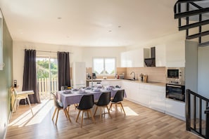 A modern kitchen with white cabinets, a built-in oven, and a dining area with a table set for four. - L'Endurance - Proche 24h du Mans (Le Mans)