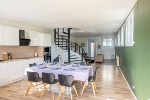 A modern kitchen with white cabinets, a built-in oven, and a black spiral staircase leading to a dining area. - L'Endurance - Proche 24h du Mans (Le Mans)
