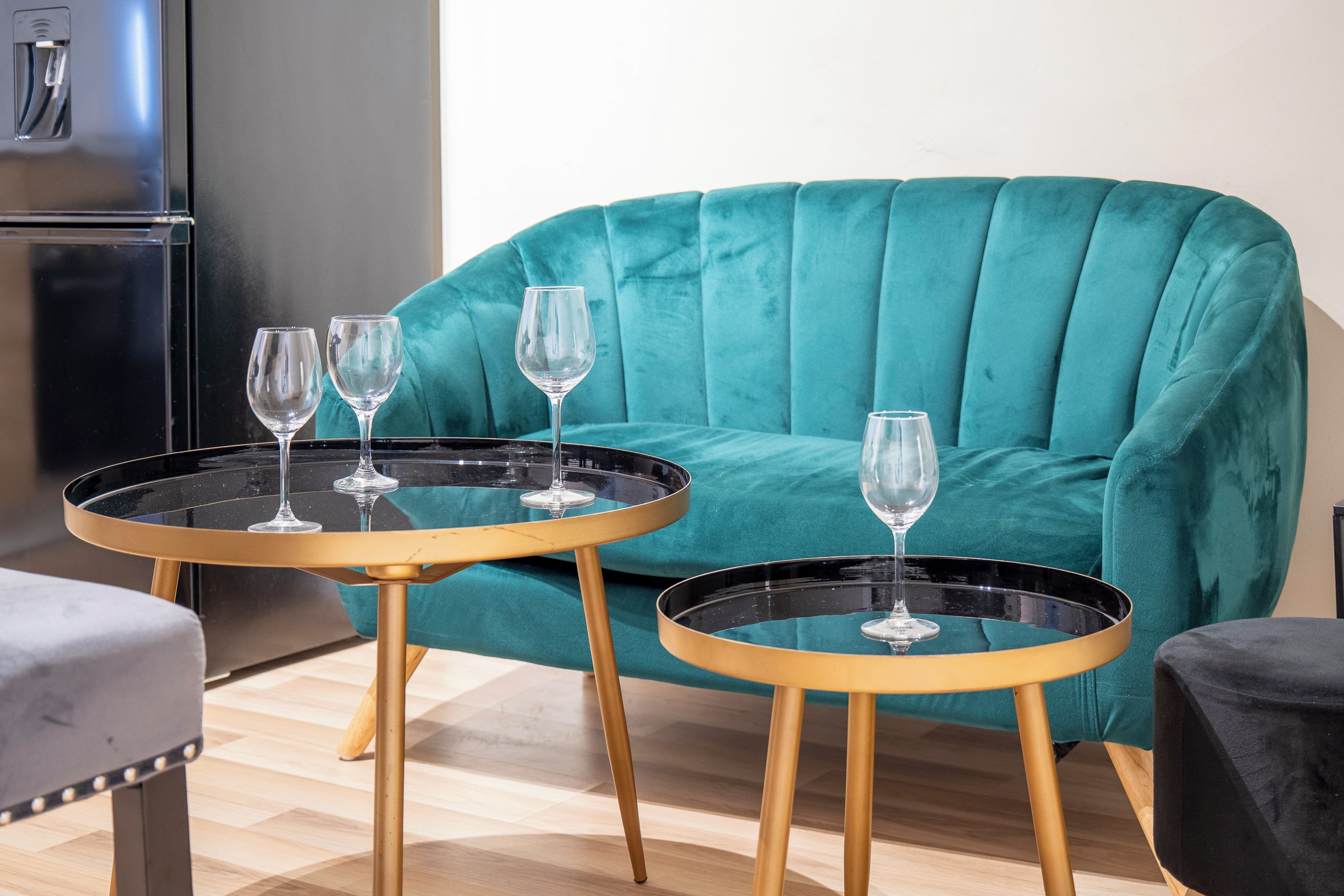 A teal armchair with a glass-top table beside it, each with a wine glass on top.