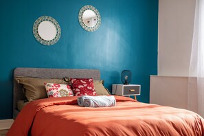 Ein Schlafzimmer mit einem Bett, Kissen, einem Nachttisch und zwei Wandspiegeln.